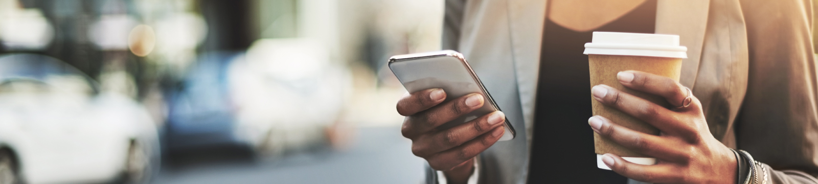 A woman using mobile phone while holding coffee